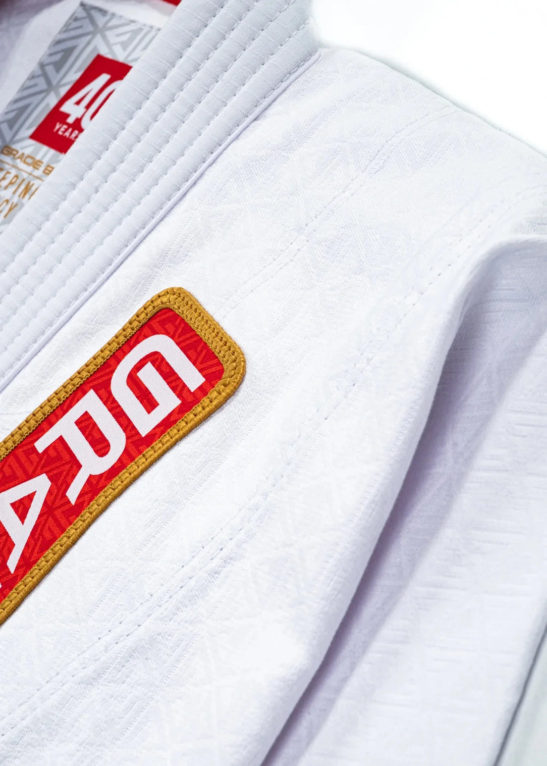 40 Year Anniversary Kimono chest detail showing Gracie Barra Patch with gold border, 40 Years collar tag, and jacquard weave