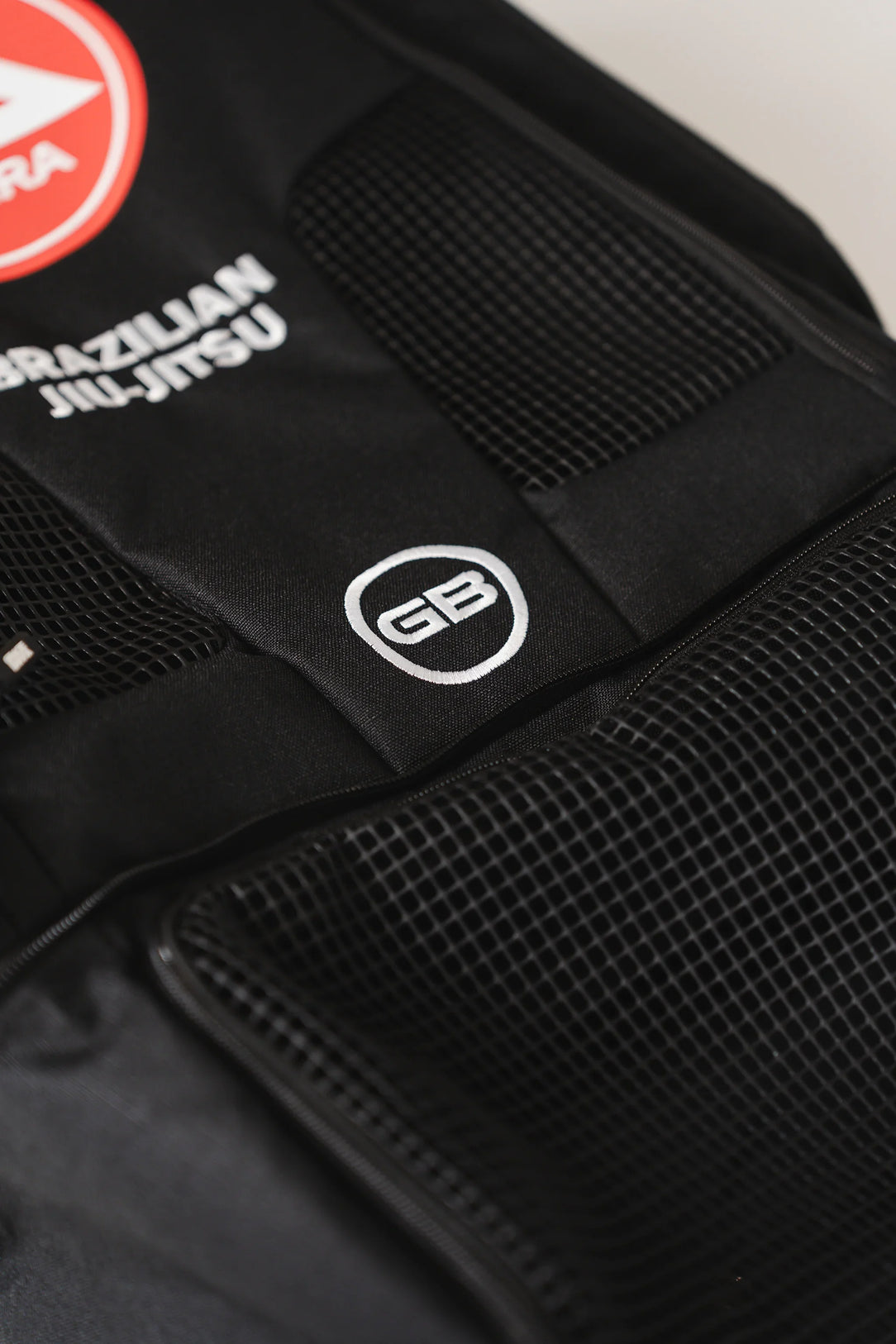 Close-up of front mesh panels on Black Barra da Tijuca Backpack showing GB circle logo embroidery and “Brazilian Jiu-Jitsu” text above the Barra shield emblem.